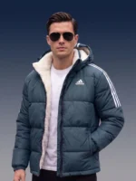 Front view of a man wearing a slate blue sherpa-lined winter puffer jacket showcasing the hood and athletic white stripes.