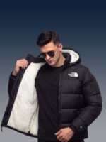 Male model wearing the unzipped black sherpa puffer jacket over a black t-shirt, highlighting the premium streetwear aesthetic and plush lining.