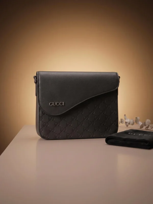 Front view of a black designer-inspired messenger bag with an embossed monogram pattern.