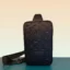 Front view of the LV inspired sling bag showcasing the black embossed artificial leather pattern and polished silver logo hardware.